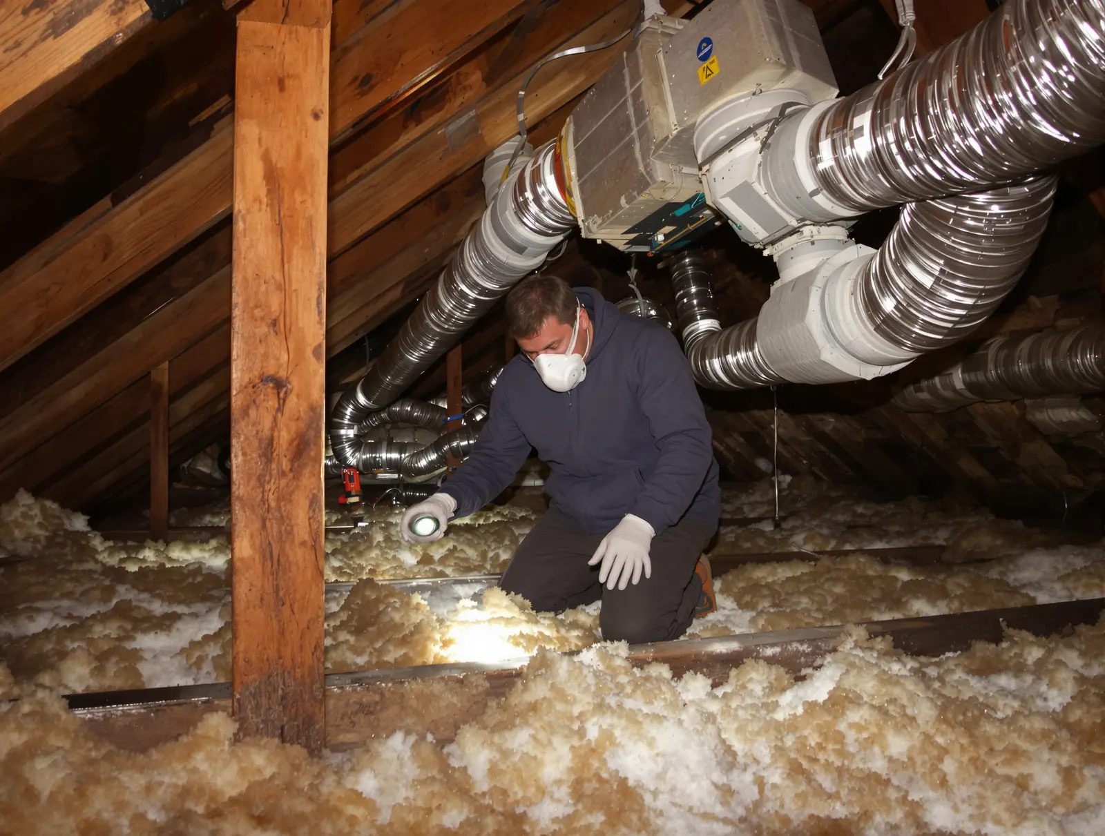 Person inspecting attic ductwork connections with a headlamp looking for gaps and damage